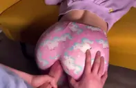 Primer plano del culo de Mía Foster con pantalón de pijama rosa de unicornios, agachada sobre el sofá amarillo mientras unas manos le agarran las nalgas